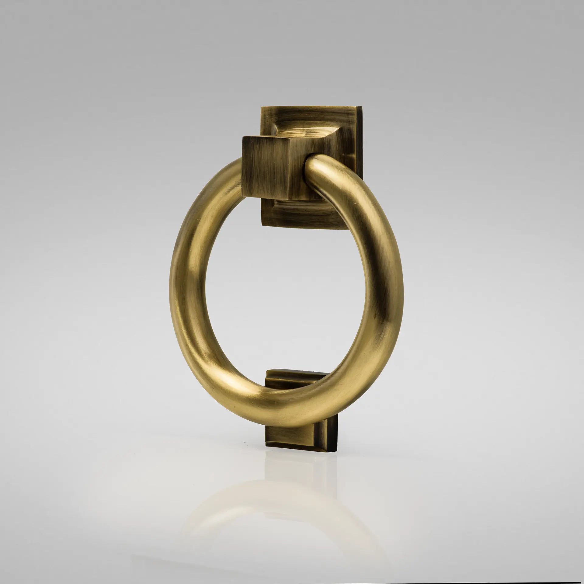 A traditional brass ring door knocker with a bold circular shape mounted on a square backplate.
