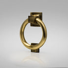 A traditional brass ring door knocker with a bold circular shape mounted on a square backplate.
